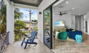 A balcony with a chair, a sofa, and a TV in the living room. - New! Beautiful beach house with heated Pool & Spa! (Holmes Beach)