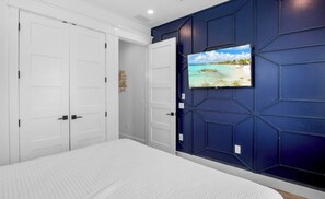 A bedroom with a bed, a TV mounted on a wall, and a wardrobe. - New! Beautiful beach house with heated Pool & Spa! (Holmes Beach)