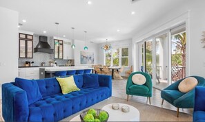 A spacious living area with a blue sofa, a dining table, and a kitchen in the background. - New! Beautiful beach house with heated Pool & Spa! (Holmes Beach)