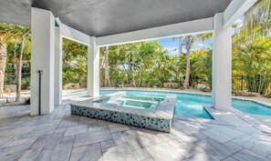Une piscine extérieure couverte, dotée d’un jacuzzi, entourée de palmiers et bordée d’un sentier en pierre.