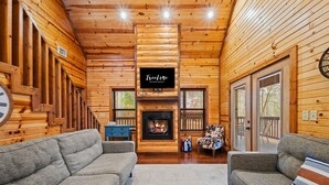 A log cabin interior with a fireplace, two sofas, a blue dresser, and a sign reading "Treeline Vacation Rental." - Couple's Retreat | Fire Pit | Hot Tub (Broken Bow)