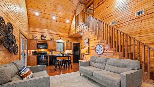 A cozy log cabin interior with a living room, kitchen, and staircase. - Couple's Retreat | Fire Pit | Hot Tub (Broken Bow)