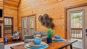 A wooden interior with a dining table set with bowls and plates, a sofa with a patterned cushion, and a wall-mounted decorative piece. - Couple's Retreat | Fire Pit | Hot Tub (Broken Bow)