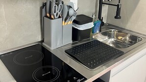 Une cuisine compacte équipée d’une plaque de cuisson à induction, d’un lave-vaisselle, d’un évier et d’une machine à café.