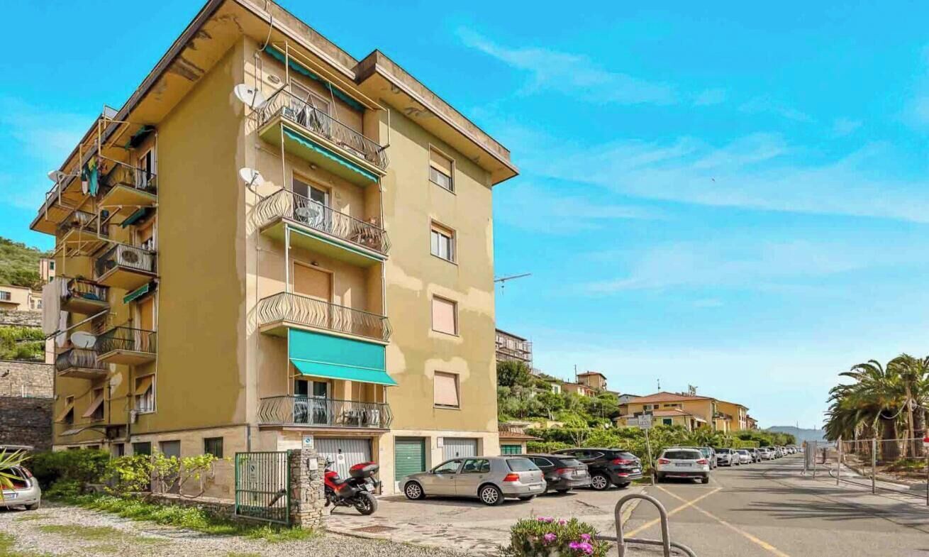 A multi-story residential building with balconies, a green awning, and parked cars.
