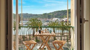 Ein Balkon mit Holztisch und zwei Stühlen, der auf einen Yachthafen mit Booten und eine hügelige Landschaft blickt.