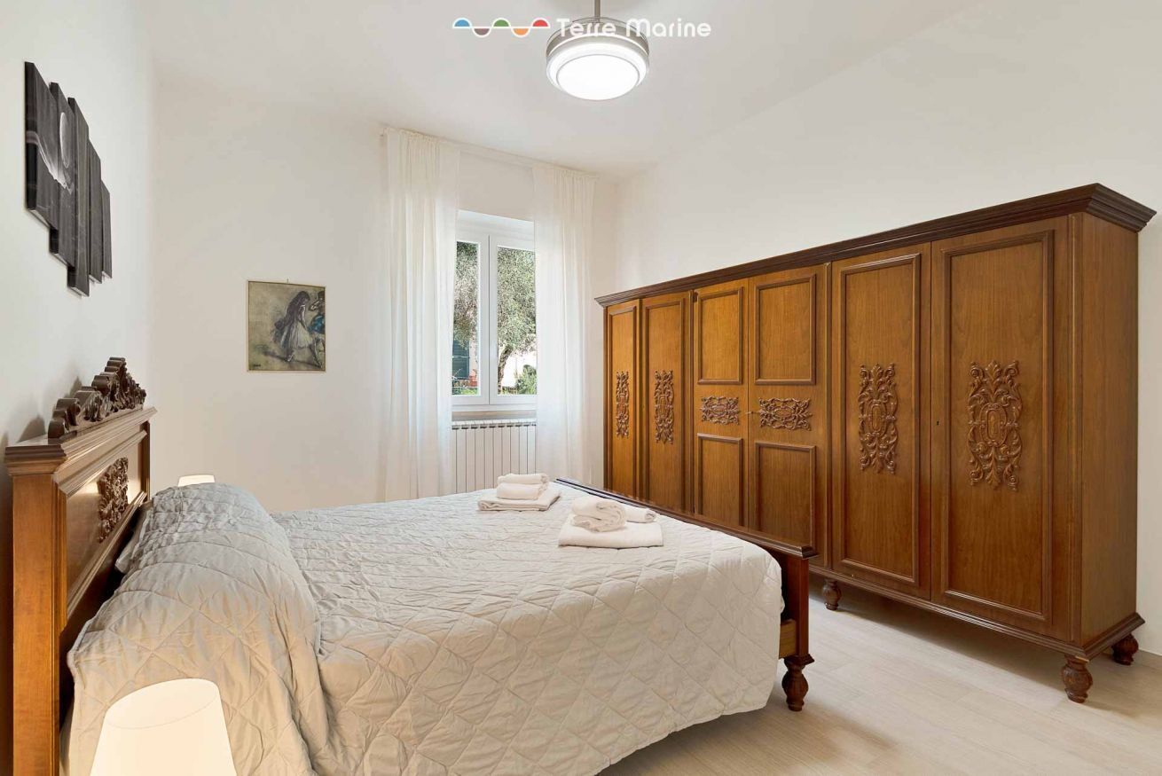 A bedroom with a large bed, a wooden wardrobe, a window with curtains, and artwork on the wall.