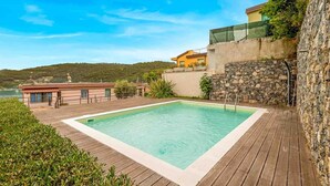 Una piscina rectangular con muelle de madera, rodeada de muros de piedra y vistas al mar.