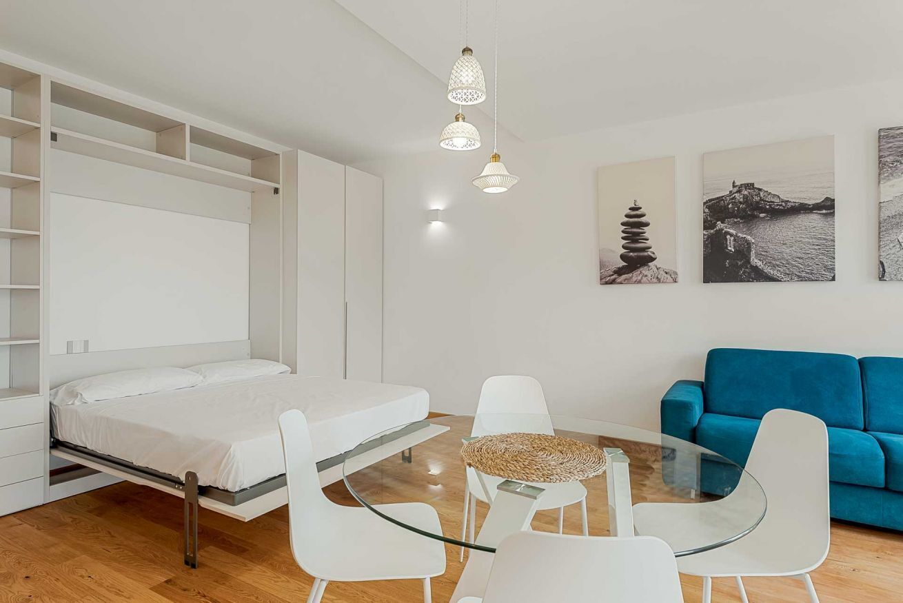 Une chambre à coucher moderne avec un lit, une table en verre, des chaises blanches, un canapé bleu et des œuvres d’art accrochées au mur.