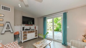 A living room with a sofa, a coffee table, a TV mounted on the wall, and a sliding glass door leading to an outdoor area. - Amazing location and location! One min. to Beach! (Holmes Beach)
