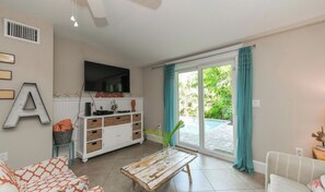 Ein Wohnzimmer mit einer Couch, einem Couchtisch, einem an der Wand befestigten Fernseher und einer Glastür zum Außenbereich.