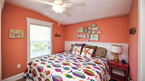 A bedroom with a bed, a ceiling fan, a window with blinds, and wall decorations. - Amazing location and location! One min. to Beach! (Holmes Beach)