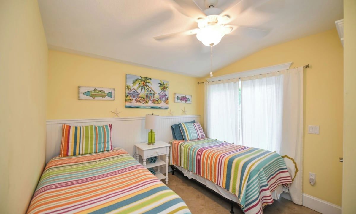 A bedroom with two beds, a ceiling fan, and a window with curtains.