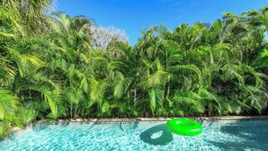 A swimming pool surrounded by lush green palm trees. - Amazing location and location! One min. to Beach! (Holmes Beach)