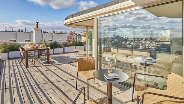 Een terras op het dak met een houten dek, een zithoek en een glazen wand met uitzicht over de stad.