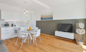 Una cocina moderna con armarios blancos, un microondas y un comedor con mesa de vidrio y sillas blancas.
