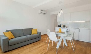 Una sala de estar moderna con un sofá gris, sillas blancas y una mesa de comedor de vidrio.