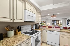 A modern kitchen with white cabinets, granite countertops, a built-in oven, and a dishwasher. - Edgewater Villas 1BR | Pools, Beach Access, & Golf (Panama City Beach)