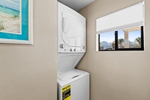 A laundry room with a washer and dryer, a window with a view, and a framed picture on the wall. - Edgewater Villas 1BR | Pools, Beach Access, & Golf (Panama City Beach)
