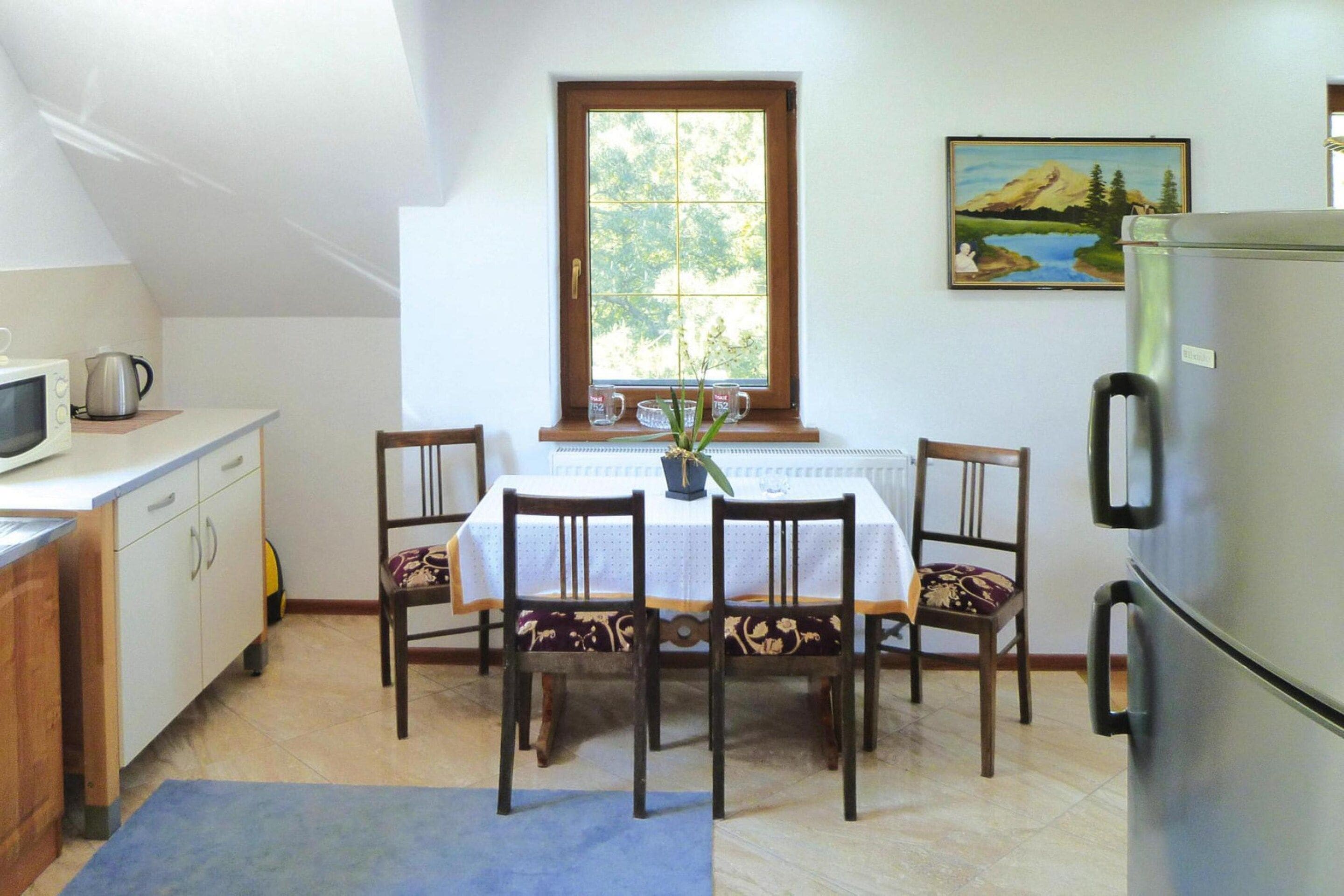 A compact kitchen with a dining table, chairs, a refrigerator, and a window with a view of greenery.