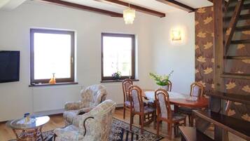 A room with a dining table, chairs, a sofa, a small round table, and a chandelier.