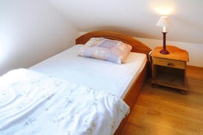 A single bed with a wooden headboard, a bedside table with a lamp, and a nightstand. - Holiday Apartment With Fireplace, Lake View (Lipnica)