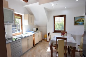 A kitchen with a dining area, a window with a view, and a painting on the wall. - Holiday Apartment With Fireplace, Lake View (Lipnica)