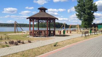 A gazebo with a roof, a swing set, and a bench area by a lake.