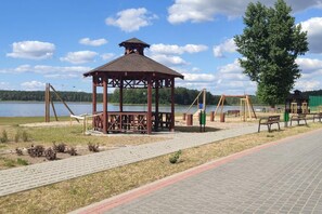 A gazebo with a roof, a swing set, and a bench area by a lake. - Holiday Apartment With Fireplace, Lake View (Lipnica)