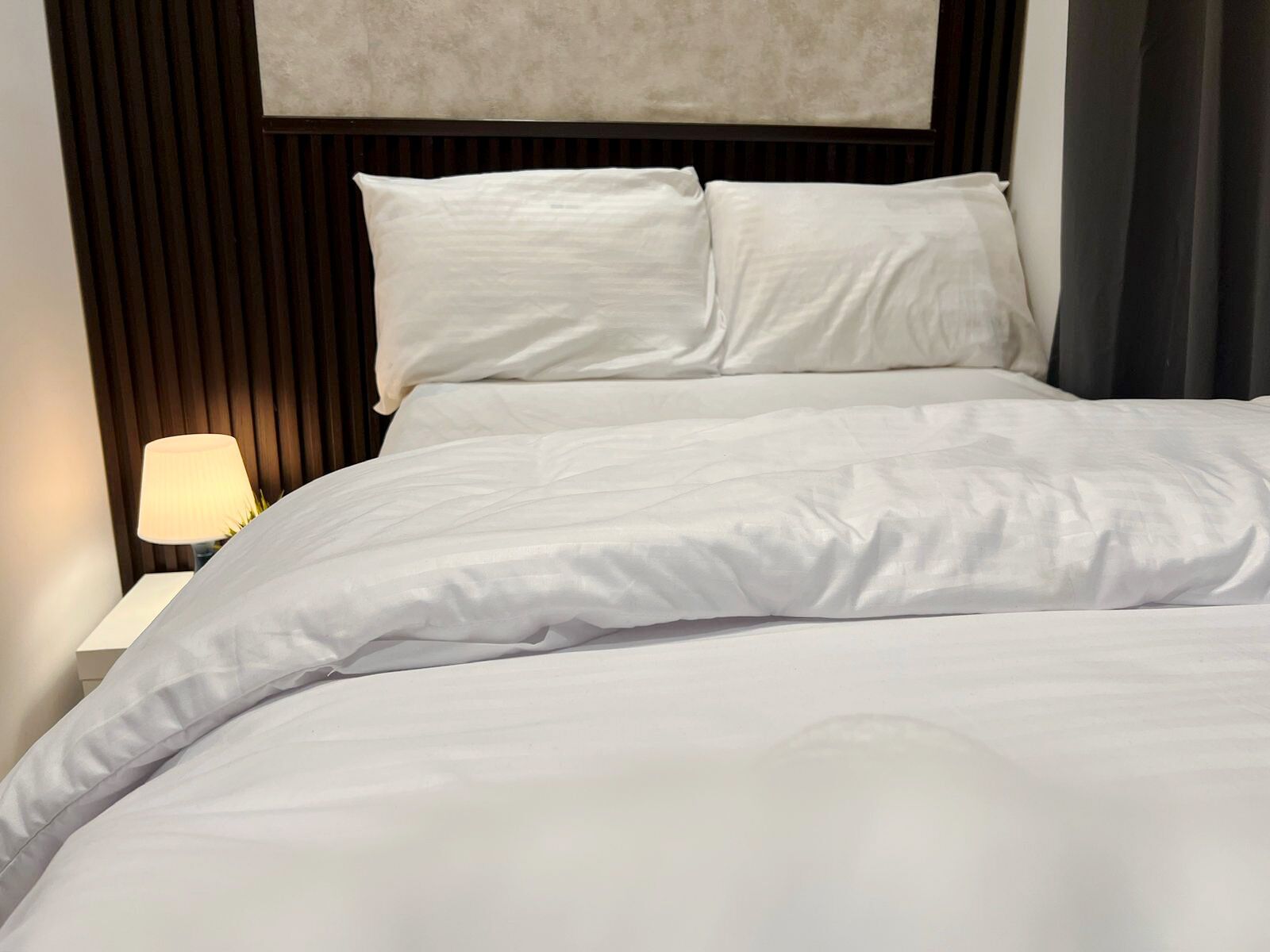 Un lit bien fait, avec du linge de lit blanc, une tête de lit sombre et une lampe de chevet.
