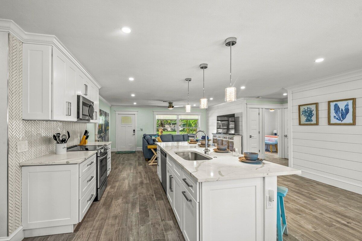 Une cuisine moderne avec des meubles blancs, un grand îlot central et des luminaires suspendus.