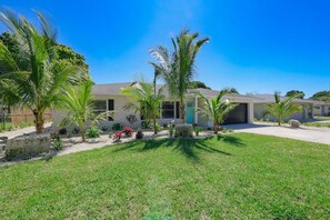 A residential property with a well-maintained lawn, palm trees, and a two-story house with a garage.