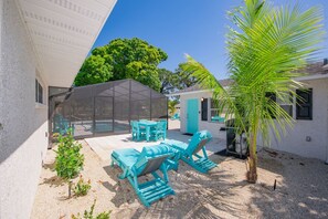 A covered outdoor seating area with a table and chairs, a palm tree, and a building with a blue door.