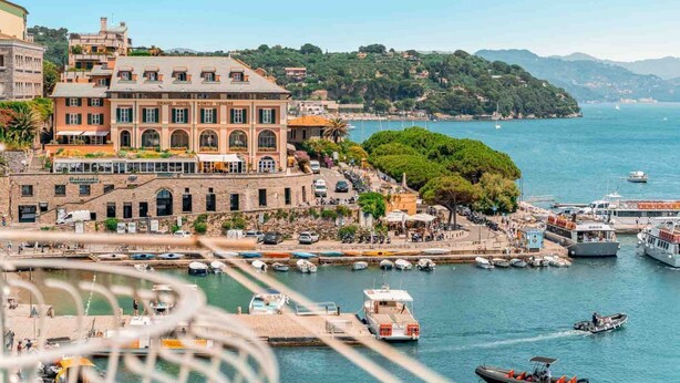 Ein Küstenhotel mit einem großen Gebäude, einer Marina mit Booten und Blick auf Meer und Hügel.