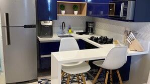 Una cuina moderna amb armaris blaus, un frigorífic d'acer inoxidable, un microones i una cuina a gas. Hi ha dues cadires blanques i una taula de dinar petita.