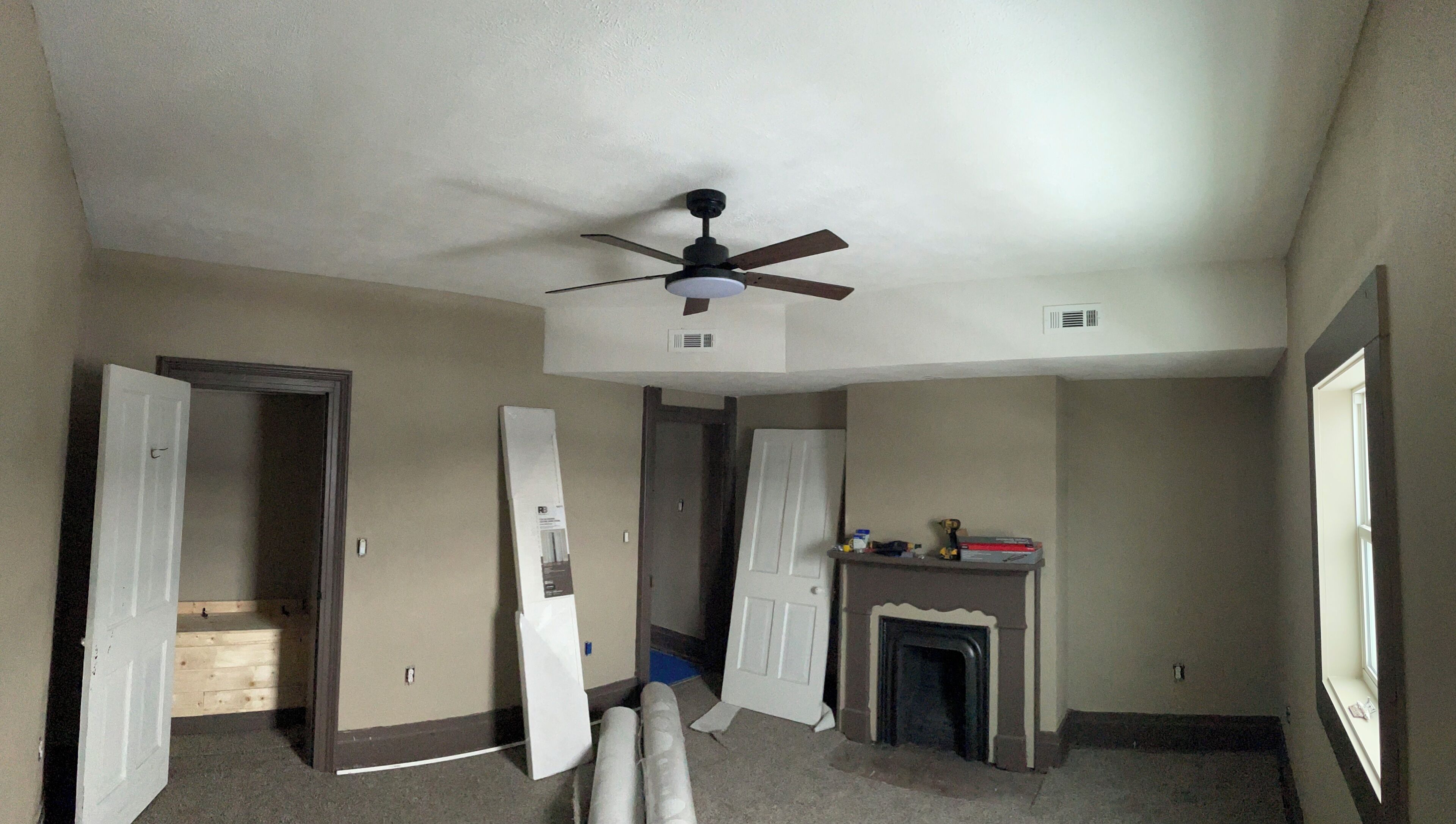 A room with a ceiling fan, a fireplace, and a door leading to another room.