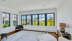 Ein geräumiges Schlafzimmer mit großen Fenstern, einem Bett, einer Bank und einem Nachttisch.