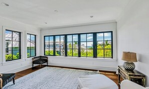 A spacious bedroom with large windows, a bed, a bench, and a nightstand. - New Beach House 1 Min to Beach! Heated Pool/Spa! (Anna Maria)