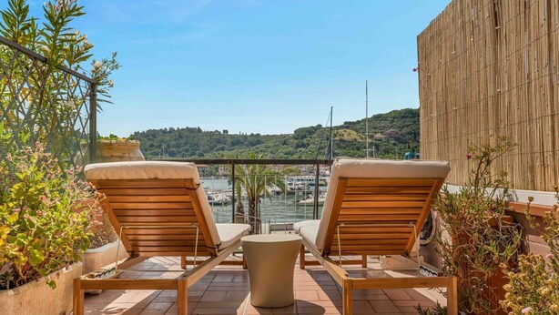 A terrace with two wooden lounge chairs and a small table, overlooking a marina and hills. - Blue Sign – Your corner of the sea in Le Grazie, PortovenereLocated in the picturesque village of Le Grazie, a hamlet of the municipality of Portovenere, Blue Sign is a holiday home with a refined and welcoming style, perfect for those looking for a re (Le Grazie)