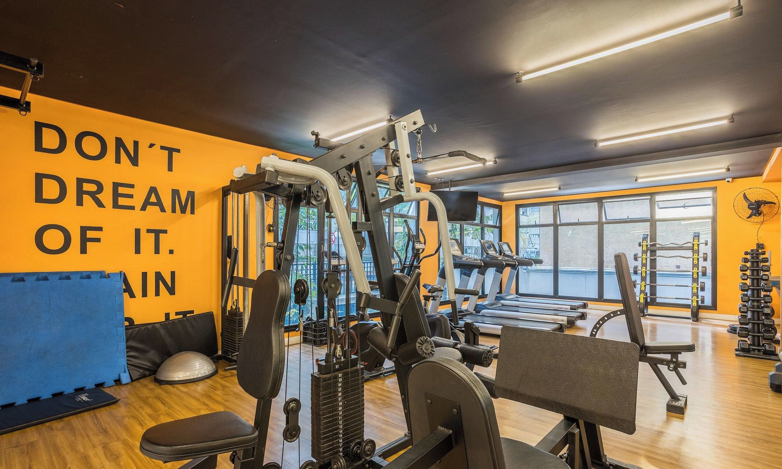 A gym with various exercise equipment, a motivational wall, and large windows.