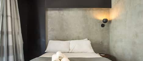 Un dormitorio moderno con una cama grande, cabecera, luz empotrada en la pared y una mesita de noche con un libro.