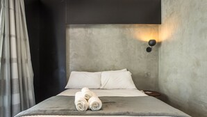 Une chambre moderne avec un grand lit, une tête de lit, une lampe fixée au mur et une table de chevet sur laquelle se trouve un livre.