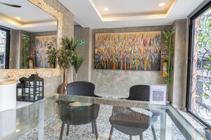 Un hall con una mesa de vidrio, dos sillas, un cuadro abstracto de colores, un espejo y una puerta con un letrero verde.