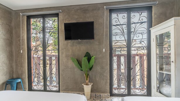A room with a bed, a TV mounted on the wall, a potted plant, and a balcony with decorative iron gates. - Casa Presentación Adaz Hotel (Santa Marta)