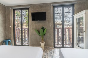 Una stanza con un letto, una televisione a parete, una pianta in vaso e un balcone con cancellate in ferro decorativo.