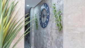 A hallway with a large wall clock, a patterned floor, and green plants. - Casa Presentación Adaz Hotel (Santa Marta)