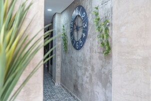 Un pasillo con un gran reloj de pared, suelo estampado y plantas verdes.