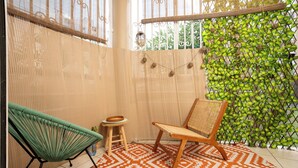 Een kamer met een kamerkleed in oranje en witte patronen, een houten stoel, een groene stoel en een klein krukje.