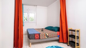 Een slaapkamer met een bed, gordijnen, een raam en een klein plankje.