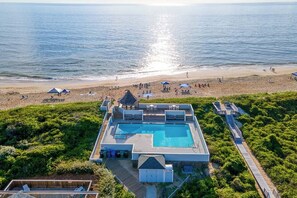 Ein Pool mit einer Sonnenterrasse, einem Strand und Blick aufs Meer.